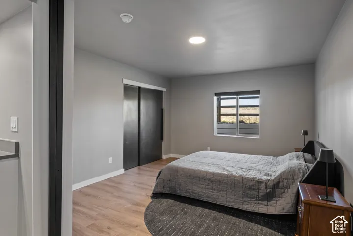 Room interior featuring wood-finish flooring, sliding dark-finish doors, recessed lighting, and a window with exterior scenery