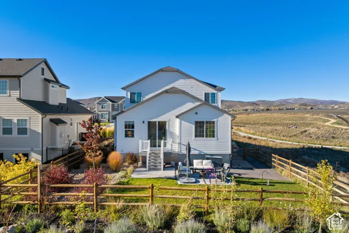 Exterior featuring white horizontal siding, raised back deck with stairs, concrete patio, and fenced backyard with mature landscaping