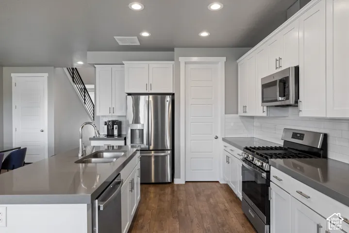 Kitchen featuring white cabinetry, solid-surface countertops, subway tile backsplash, stainless steel appliances, and wood-finish flooring