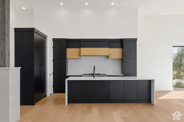 Kitchen featuring custom two-tone cabinetry, waterfall-edge island, wood-finish flooring, and recessed ceiling lighting