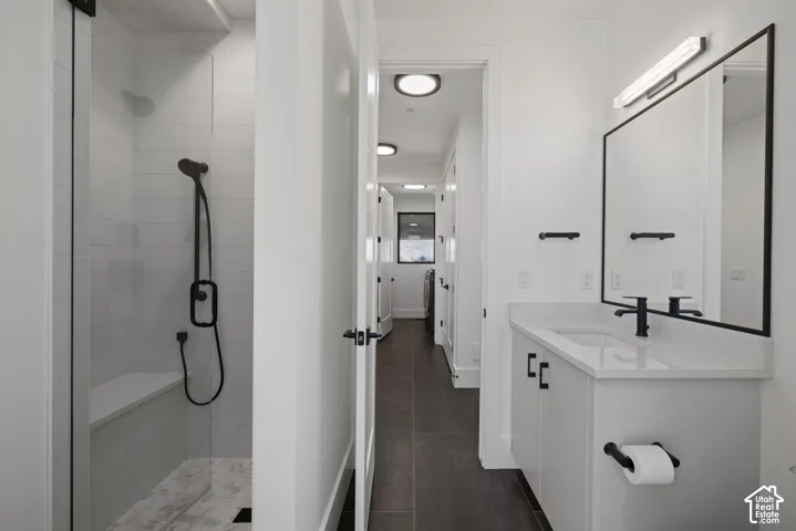 Bathroom featuring a vanity with a light-toned countertop, rectangular undermount sink, matte black faucet, and framed mirror with integrated lighting, paired with a glass-enclosed shower featuring tile surrounds and a built-in bench