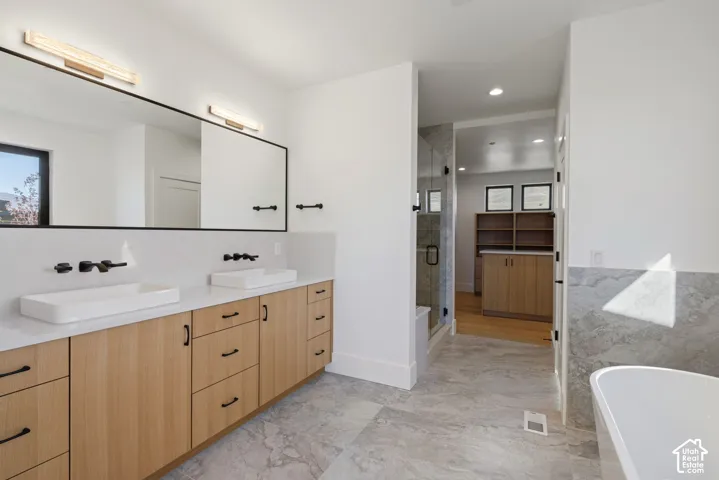 Double vanity featuring wood-finish cabinetry, rectangular vessel sinks, matte black wall-mounted faucets, stone-finish tile flooring, and a freestanding soaking tub