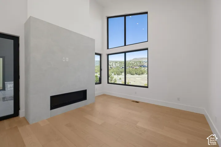 Double-height ceiling, large windows with natural scenery, stone-finish fireplace surround, wood-finish flooring, and black-framed glass exterior door