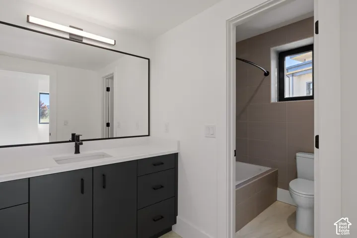 Modern vanity featuring dark cabinetry, white countertop, integrated rectangular sink, and matte black hardware, paired with a large wall-mounted mirror, linear LED vanity lighting, and a tile-surround bathtub