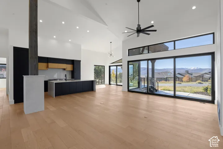 Open-concept interior featuring vaulted ceilings, wide-plank wood-finish flooring, floor-to-ceiling sliding glass doors, a kitchen island with stone surfacing, and integrated black cabinetry