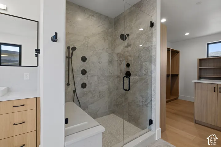 Walk-in shower featuring floor-to-ceiling stone-finish wall tile, frameless glass enclosure, matte black multi-head fixtures, integrated bench seat, and pebble-finish flooring