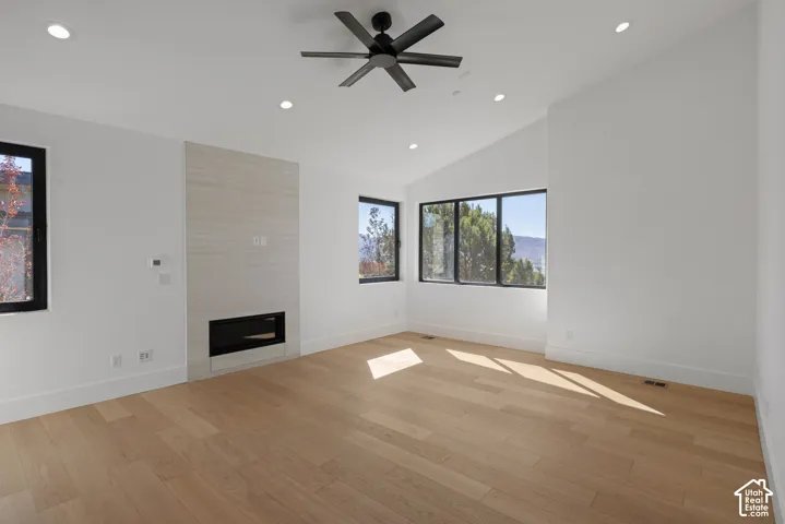 Vaulted ceiling featuring recessed lighting and a matte black ceiling fan, wood-finish flooring, and a linear fireplace with a textured surround