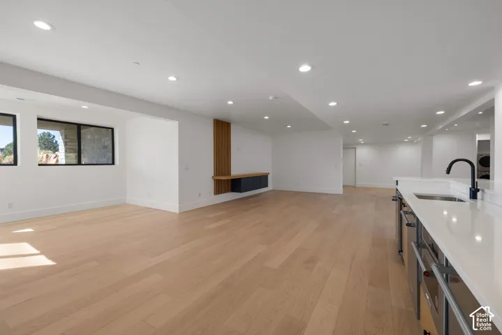Open-concept interior featuring light wood-finish flooring, recessed lighting, a floating wall-mounted console with vertical wood slat detailing, and a kitchen island with stone-surface countertop and matte black hardware