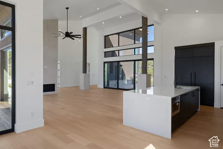 Open-concept interior featuring vaulted ceilings, floor-to-ceiling windows, wood-finish flooring, a stone-surround fireplace, and a center island with a stone countertop