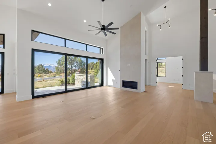Vaulted ceilings with wood-finish flooring, floor-to-ceiling multi-panel sliding glass doors, built-in horizontal fireplace with stone surround, modern industrial ceiling fan, and multi-arm chandelier lighting