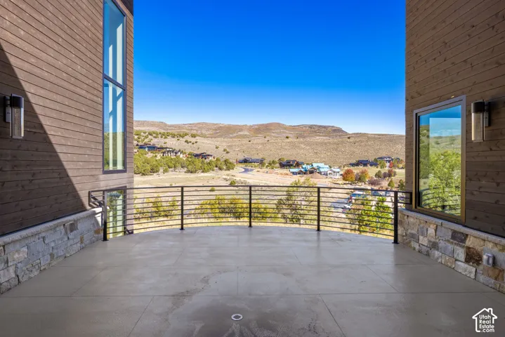 Covered terrace featuring horizontal metal railing, stone masonry base, wood-finish siding, vertical windows, and mountain scenery