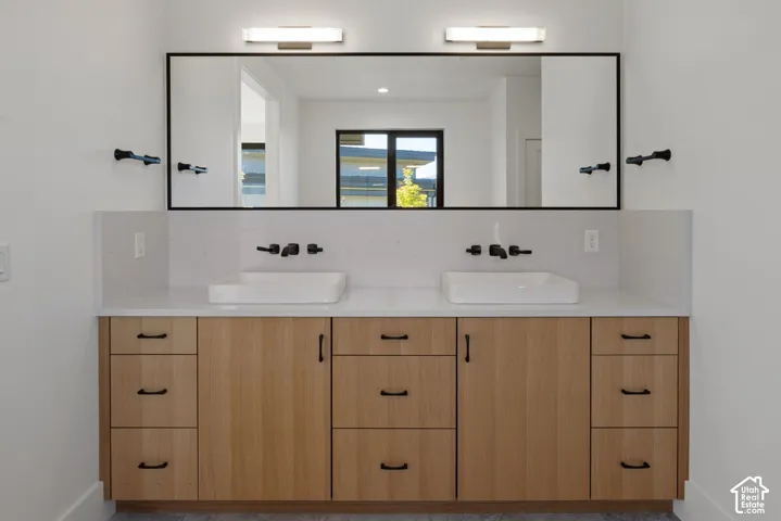 Double vanity featuring light-toned wood cabinetry, stone-composite countertops, rectangular vessel sinks, matte black wall-mounted faucets, and a large black-framed mirror