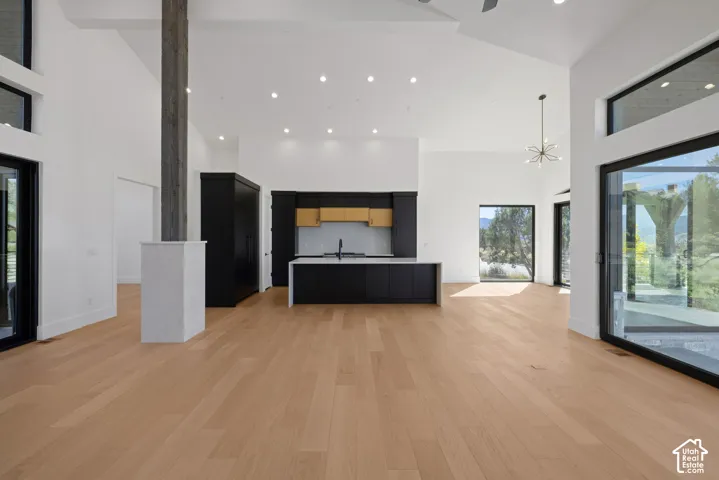 Open-concept interior featuring vaulted ceilings, wide-plank wood-finish flooring, a kitchen island with stone countertops, floor-to-ceiling glass sliding doors, and a central structural timber post