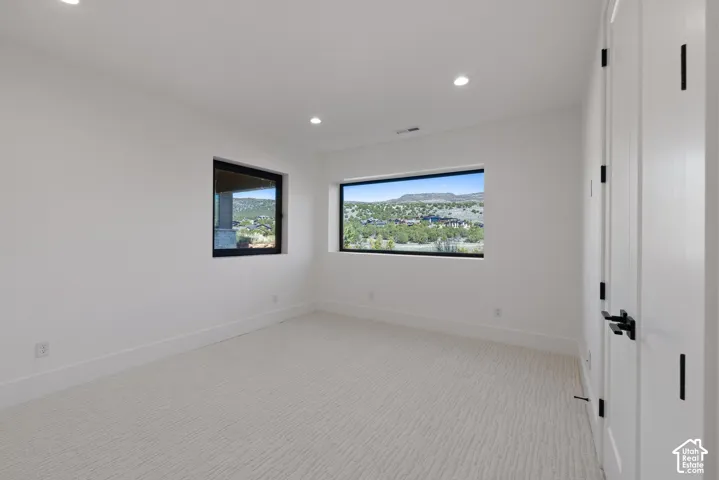 Bright interior space featuring recessed lighting, textured carpet flooring, expansive windows with dark frames, and white doors with matte black hardware