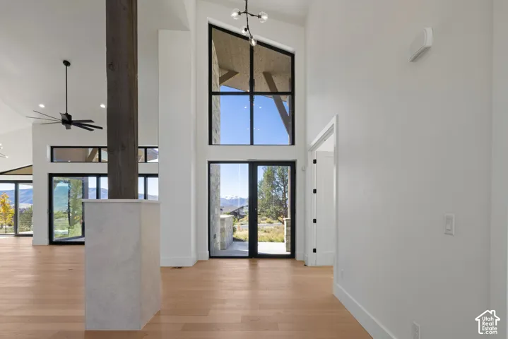 Vaulted ceiling featuring floor-to-ceiling windows with black frames, wood-finish flooring, exposed timber structural column, and custom multi-light chandelier