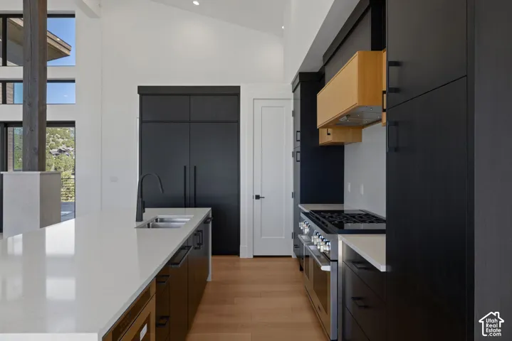 Modern kitchen featuring flat-panel matte black cabinetry, light wood-finish upper cabinets, expansive quartz countertops, a professional-grade stainless steel gas range, and wood-finish flooring