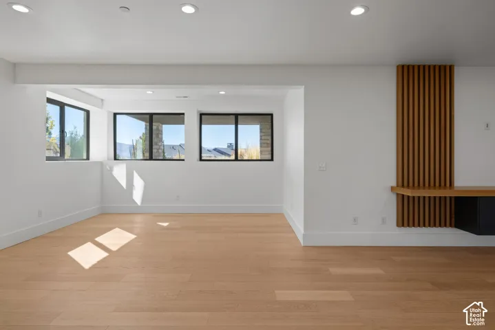 Wood-finish flooring, recessed lighting, expansive windows with dark frames, and a vertical wood-slat accent wall with a built-in floating shelf