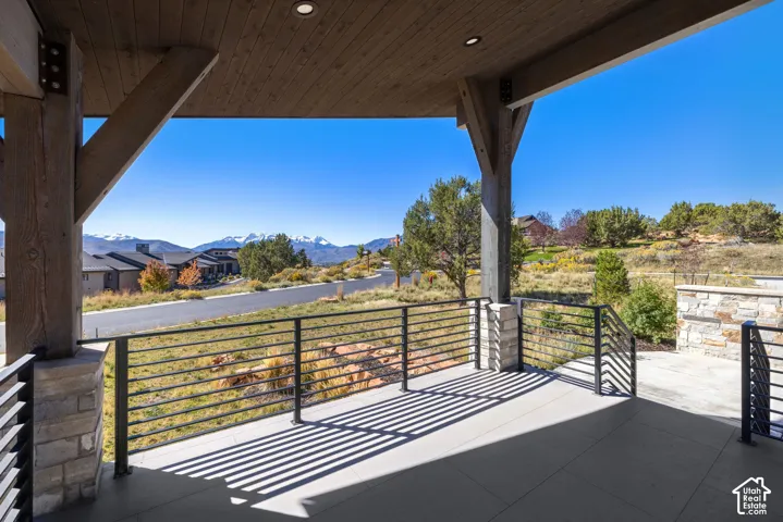 Covered patio featuring timber beam support structures, recessed lighting, tile flooring, metal horizontal railing, and stone pillar bases