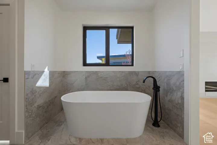 Freestanding soaking tub with a matte black floor-mounted faucet, surrounded by large-format gray stone-tile wall and floor cladding