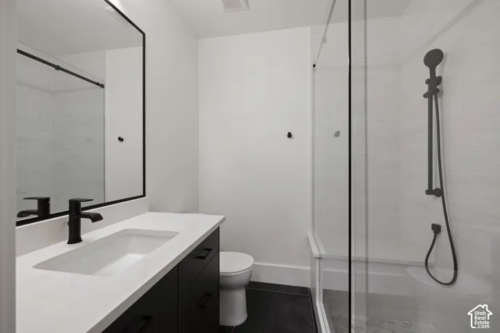 Bathroom featuring a vanity with a white countertop and matte black hardware, a rectangular undermount sink, a framed mirror, and a walk-in shower with a glass enclosure and a matte black handheld showerhead