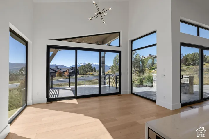 Vaulted ceiling featuring a multi-arm geometric chandelier, floor-to-ceiling windows, wide-plank wood-finish flooring, and multiple sliding glass doors opening to an exterior patio
