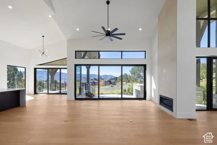 Vaulted ceilings with recessed lighting, floor-to-ceiling stone-clad fireplace, expansive black-framed sliding glass doors, wood-finish flooring, and multi-light pendant chandelier
