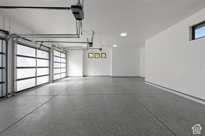 Spacious multi-car garage featuring epoxy-coated flooring, frosted glass-panel doors, ceiling-mounted automatic door openers, recessed LED lighting, and multiple clerestory windows