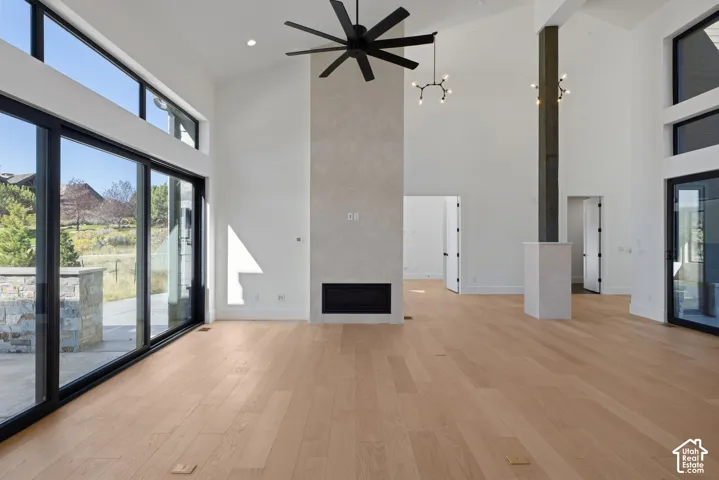 Vaulted ceilings featuring a full-height stone fireplace surround, wide-plank wood-finish flooring, floor-to-ceiling sliding glass doors, a large-scale ceiling fan, and a structural pillar with stone base