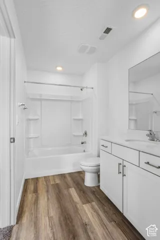 Bathroom featuring wood-finish flooring, white cabinetry with silver-tone hardware, a solid-surface countertop with an integrated sink, and a combination tub and shower enclosure with recessed shelving