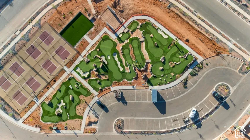 Aerial view of community recreational space featuring a multi-hole miniature golf course, four fenced courts, designated paved parking area, and synthetic turf lawn