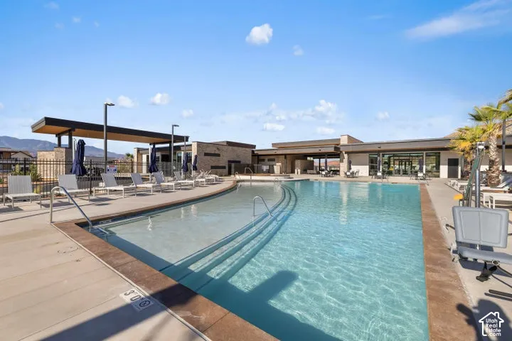 Swimming pool featuring a zero-entry design, concrete deck, metal perimeter fencing, and covered patio structures