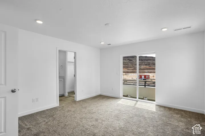 Neutral interior space featuring recessed ceiling lighting, wall-to-wall carpeting, sliding glass doors, and a balcony with a mountain backdrop