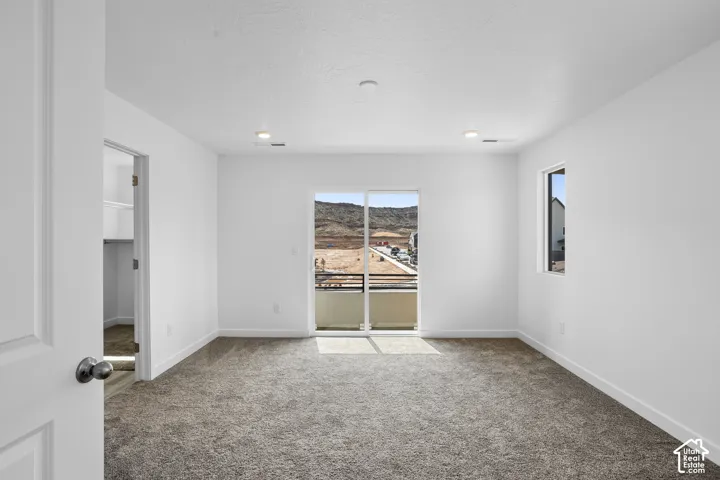 Room featuring neutral carpeting, recessed ceiling lighting, a walk-in closet, and sliding glass doors with access to a railed balcony