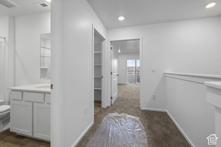 Bathroom vanity with white cabinetry and solid surface countertop, recessed lighting, carpeted flooring, and walk-in closet with built-in shelving
