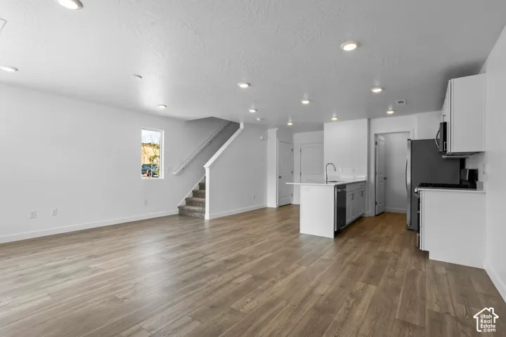 Open-concept floor plan featuring wood-finish flooring, recessed lighting, white cabinetry, and an island with a stainless steel sink