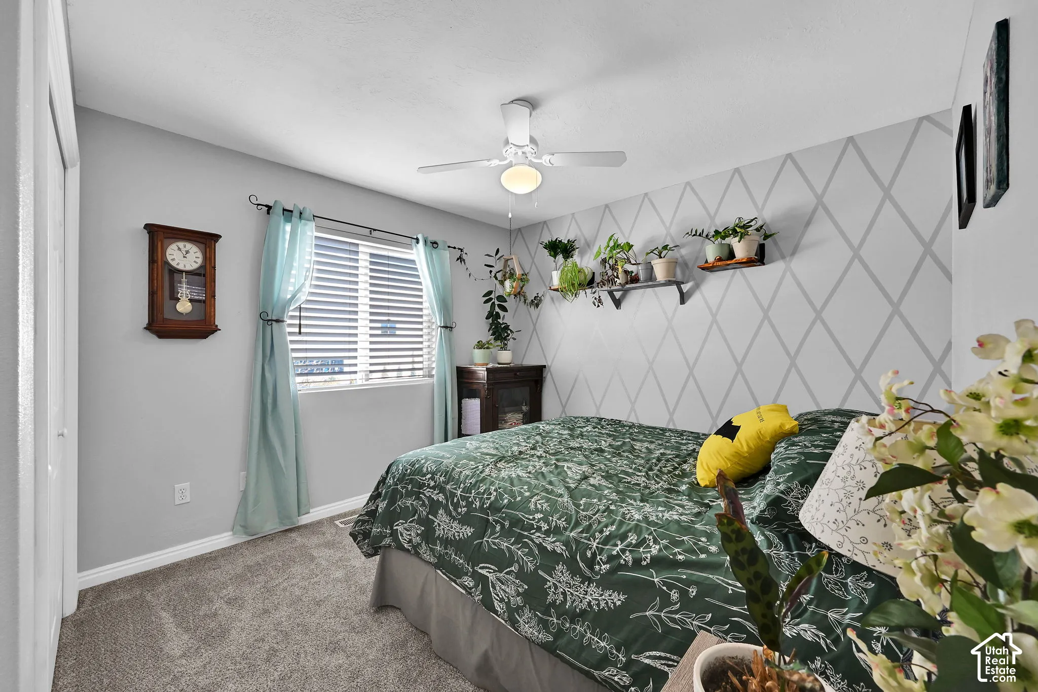 Neutral carpeted flooring, diamond-patterned accent wall, central ceiling fan with integrated lighting, and horizontal window blinds
