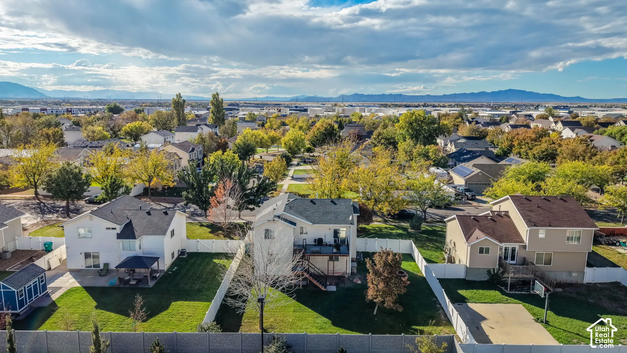 Aerial perspective featuring residential lots with fenced perimeters, expansive lawns, elevated wooden decks, and mountain range backdrop
