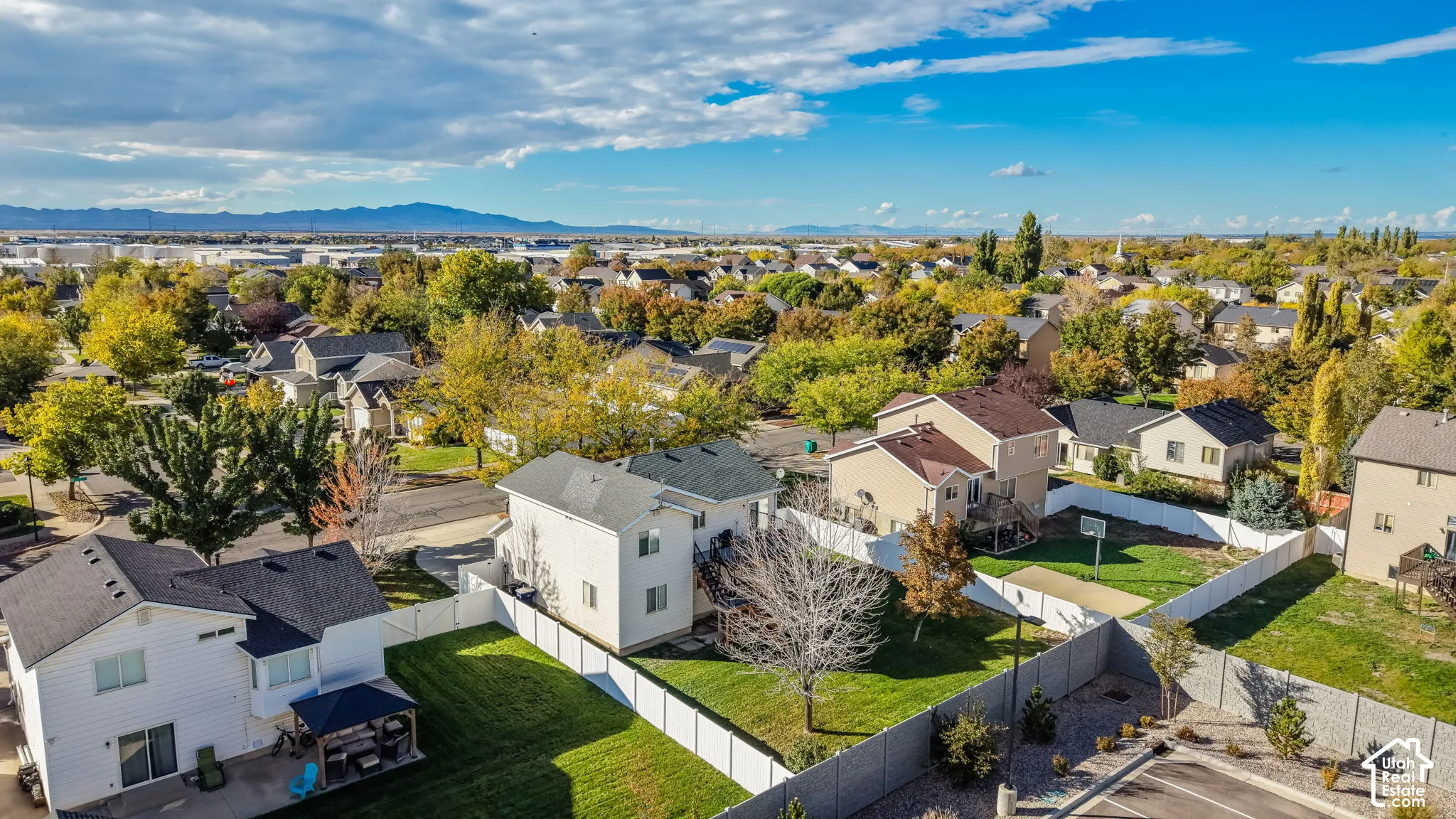 Aerial perspective featuring residential properties with manicured lawns, white vinyl fencing, and mountain horizon backdrop