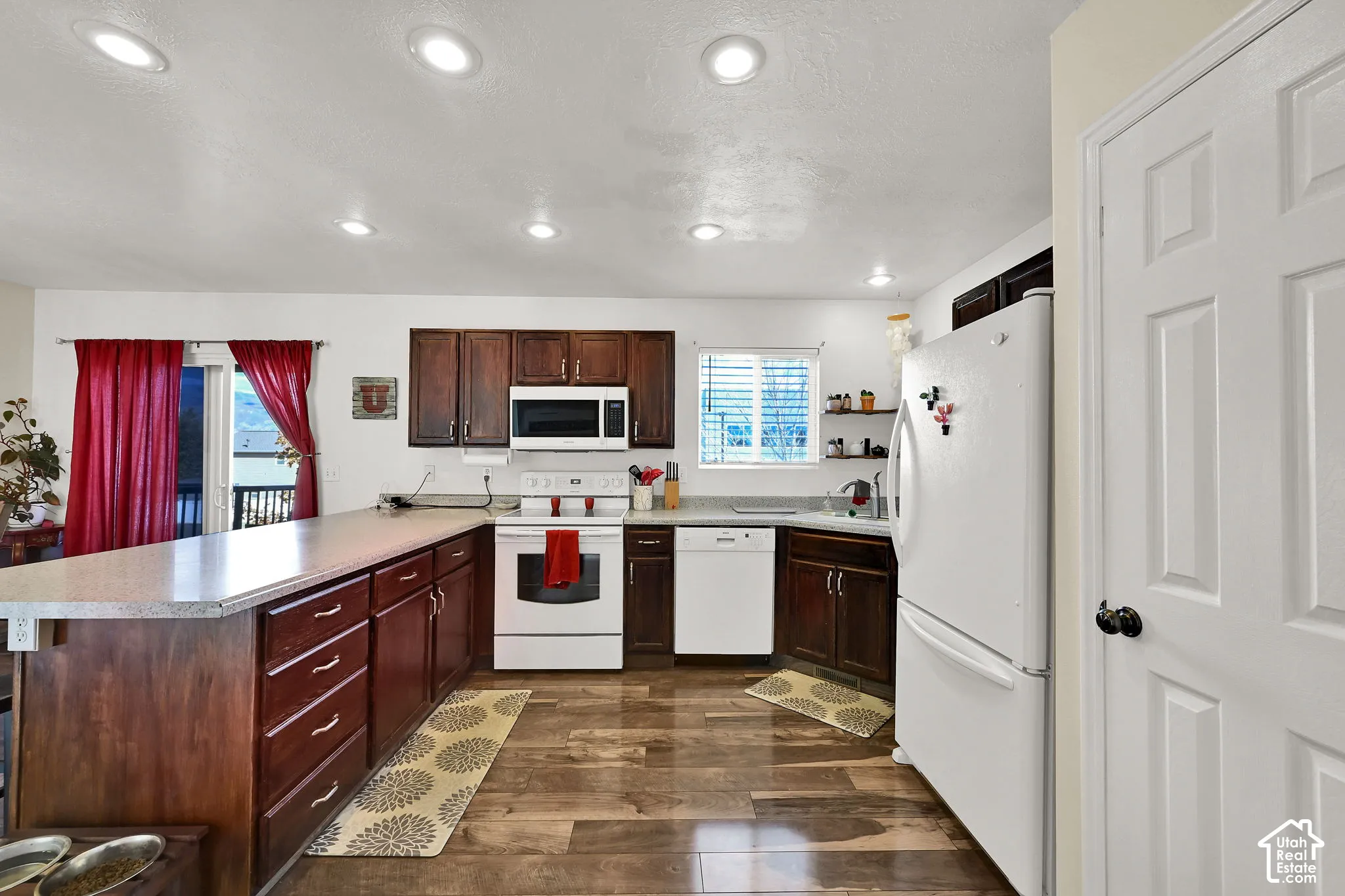Kitchen featuring dark-toned cabinetry, a peninsula countertop, wood-finish flooring, recessed ceiling lighting, and built-in appliances