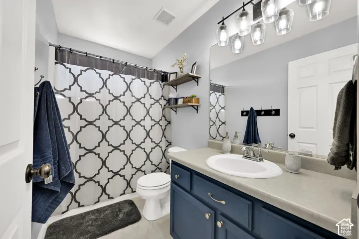 Bathroom featuring a navy blue vanity cabinet, neutral solid-surface countertop with an integrated basin, large wall-mounted mirror, and multi-bulb decorative light fixture