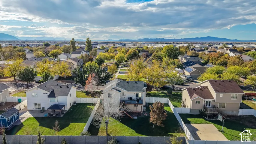 Aerial perspective featuring residential lots with fenced perimeters, expansive lawns, elevated wooden decks, and mountain range backdrop