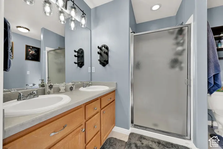 Bathroom featuring a dual-sink vanity with a solid-surface countertop, wood cabinetry, a walk-in shower with a frosted glass door, and multi-light pendant vanity lighting