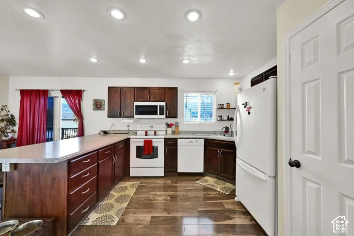 Kitchen featuring dark-toned cabinetry, a peninsula countertop, wood-finish flooring, recessed ceiling lighting, and built-in appliances