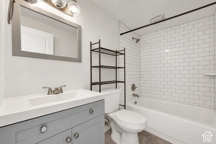 Bathroom featuring a gray shaker-style vanity with a solid surface countertop, white subway tile shower surround, and a framed mirror with integrated vanity lighting