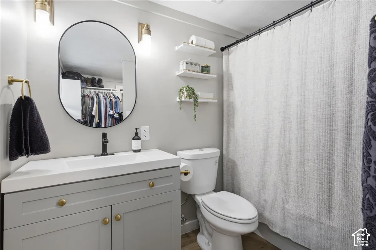 Grey shaker-style vanity with integrated rectangular sink and gold-tone hardware, paired with a matte black faucet, oval wall-mounted mirror, and wall-mounted light fixtures