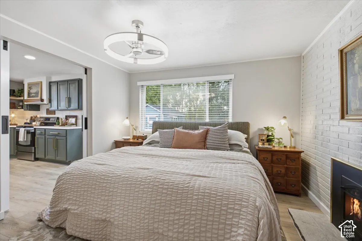 Painted brick accent wall featuring a black metal fireplace surround, modern circular LED ceiling light fixture, wood-finish flooring, and horizontal window blinds
