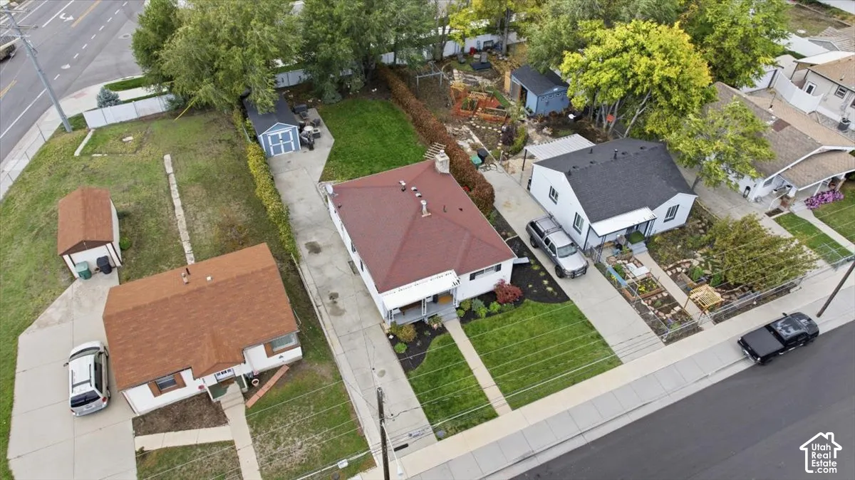Aerial view featuring a detached residence with a hipped roof, concrete driveway, front lawn, and a backyard with an accessory storage structure