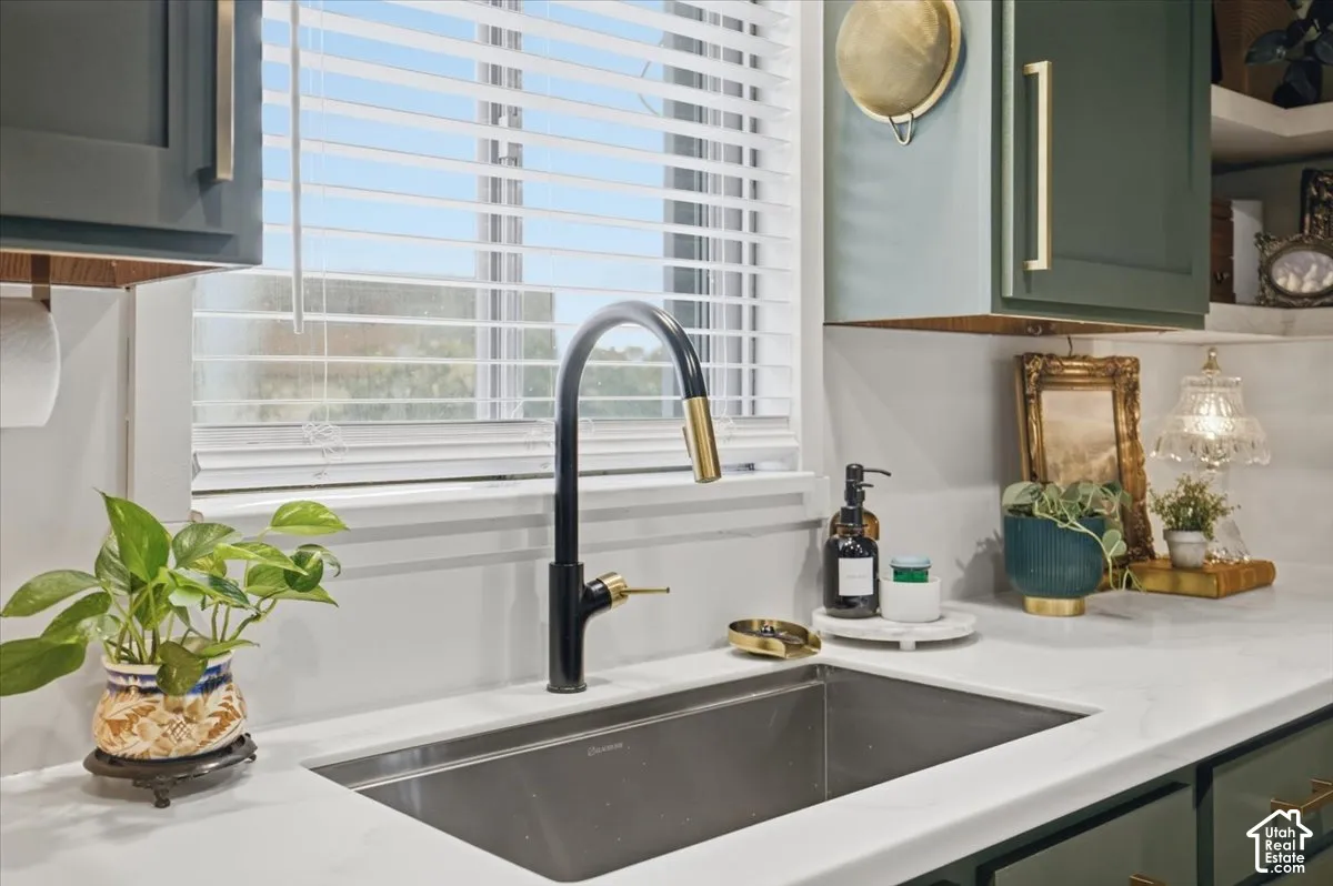 Undermount stainless steel kitchen sink featuring a dual-tone, high-arc pull-down faucet, white solid-surface countertops, and matte finish cabinetry with gold-tone hardware