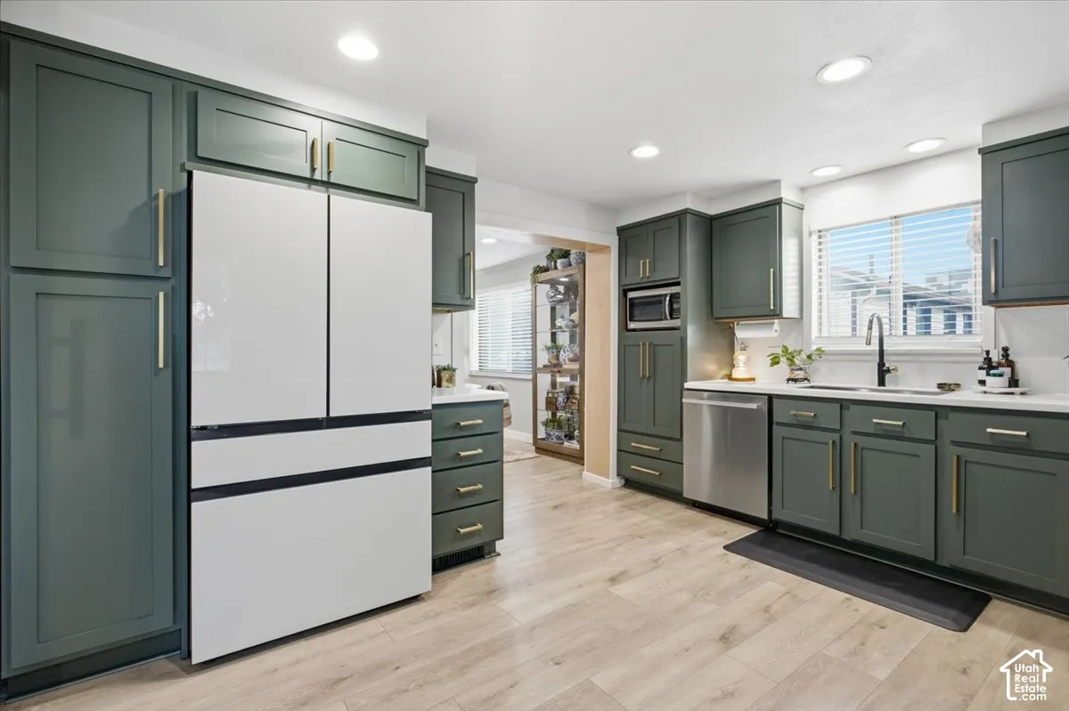 Kitchen featuring forest green shaker-style cabinetry, gold-tone hardware, wood-finish flooring, recessed lighting, and a stainless steel dishwasher