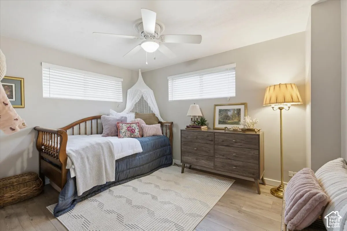 Neutral interior space featuring wood-finish flooring, two windows with horizontal blinds, and a white ceiling fan with integrated lighting